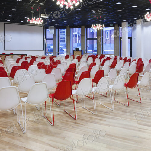 Large empty room with red and white chairs in rows, ready for a presentation