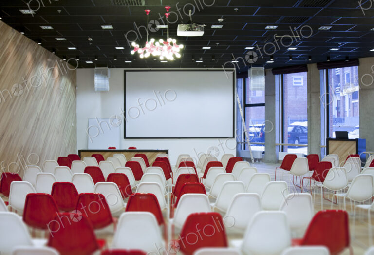 Large empty room with red and white chairs in rows, ready for a presentation