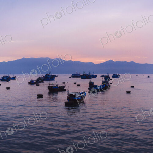 Large group of fisherman in traditional fishing boats on lake at sunrise, mountains in… Large group of fisherman in traditional fishing boats on lake at sunrise, mountains in…