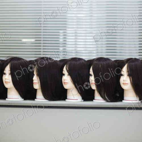 Large group of mannequin heads with brown wigs in a row on a table. Large group of mannequin heads with brown wigs in a row on a table.