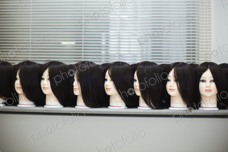 Large group of mannequin heads with brown wigs in a row on a table.