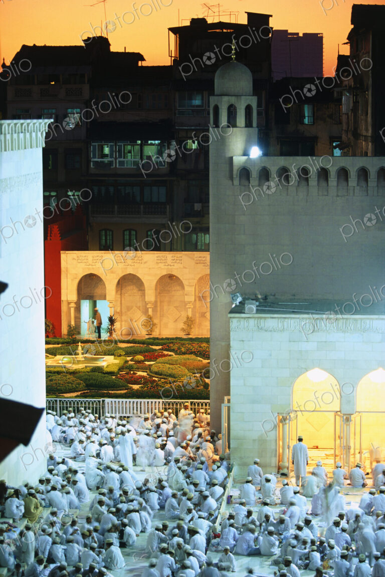 Large group of men gathered around mosque at dusk.
