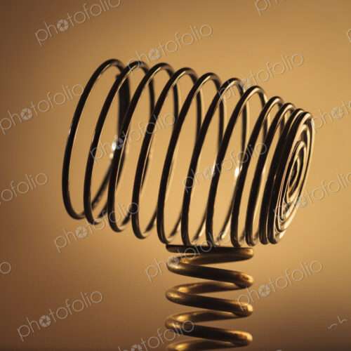 Large metal coiled spring balancing on a smaller spring, studio shot. Large metal coiled spring balancing on a smaller spring, studio shot.