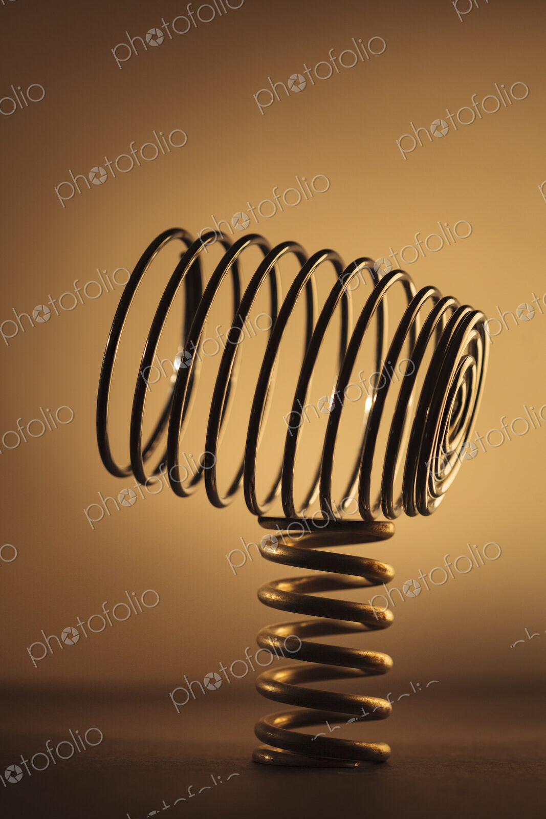 Large metal coiled spring balancing on a smaller spring, studio shot.