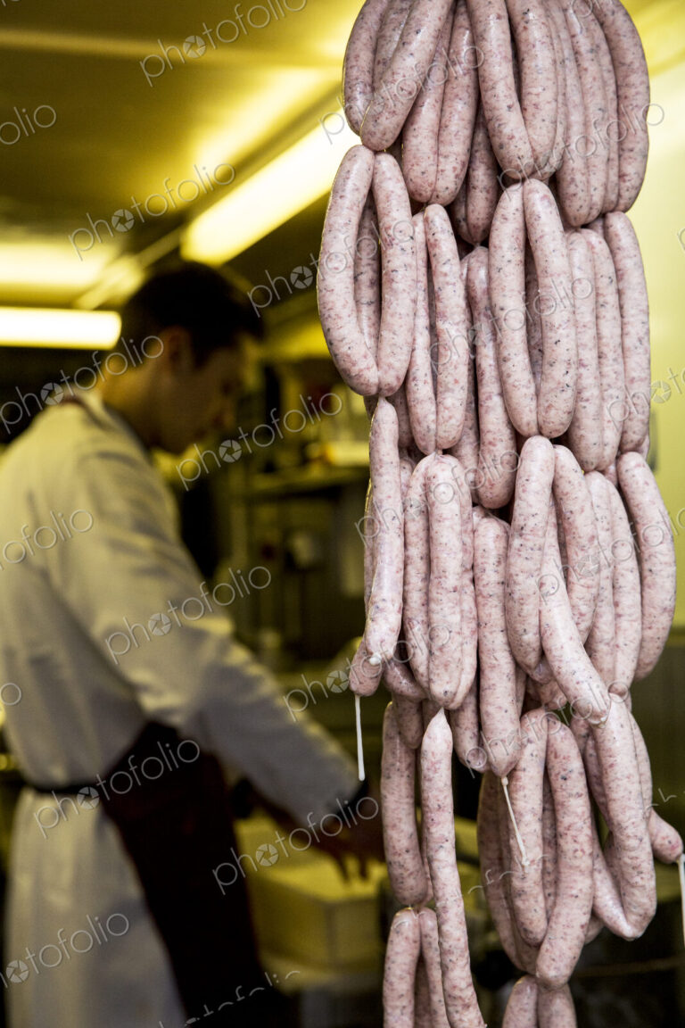 Large number of freshly made sausages hanging in a butcher shop, man wearing apron…