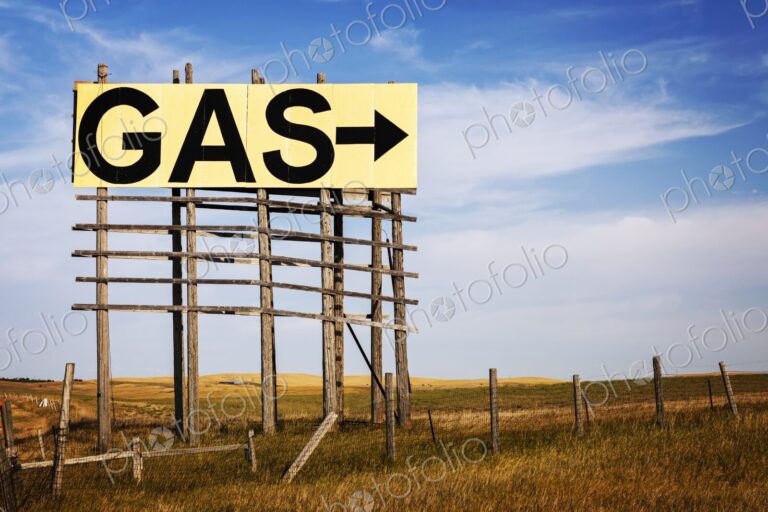 Large roadside GAS arrow sign on a weathered wooden billboard stands in a rural…