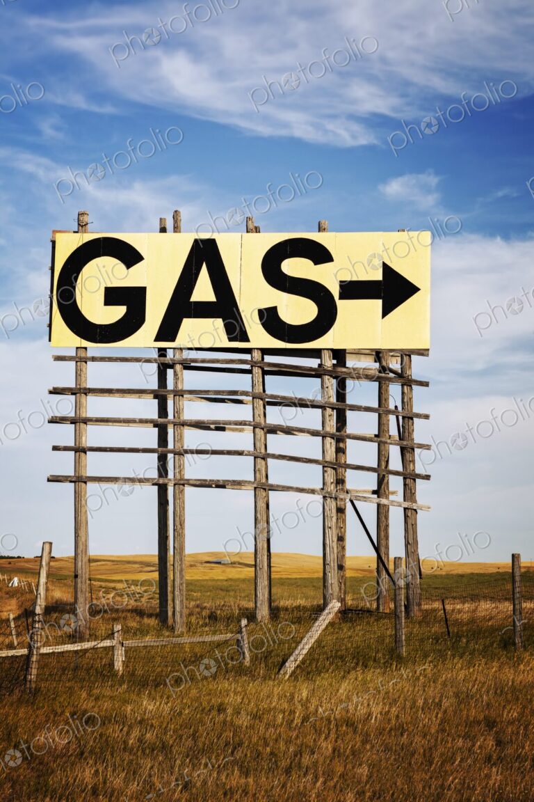 Large roadside GAS arrow sign on a weathered wooden billboard stands in a rural…