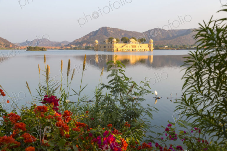 Large water palace in the middle of a lake, red flowers in the foreground.