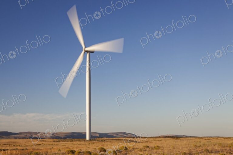 Large wind turbine spins in an open Oregon landscape with clear blue sky and golden…