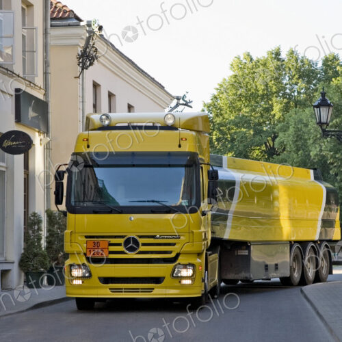 Large yellow truck in a narrow street, taking a corner, a fuel tanker.