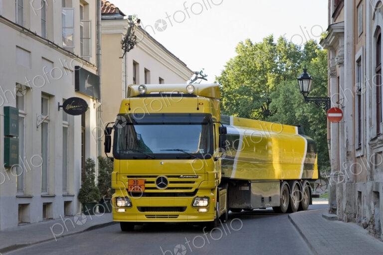 Large yellow truck in a narrow street, taking a corner, a fuel tanker.