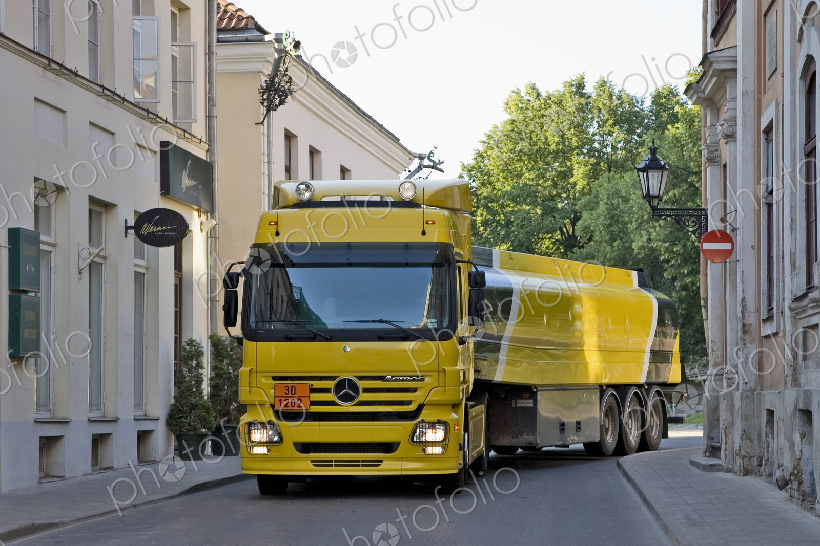Large yellow truck in a narrow street, taking a corner, a fuel tanker.