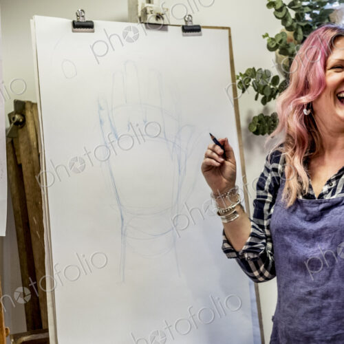 Laughing woman wearing apron standing at an easel, drawing of human hand.