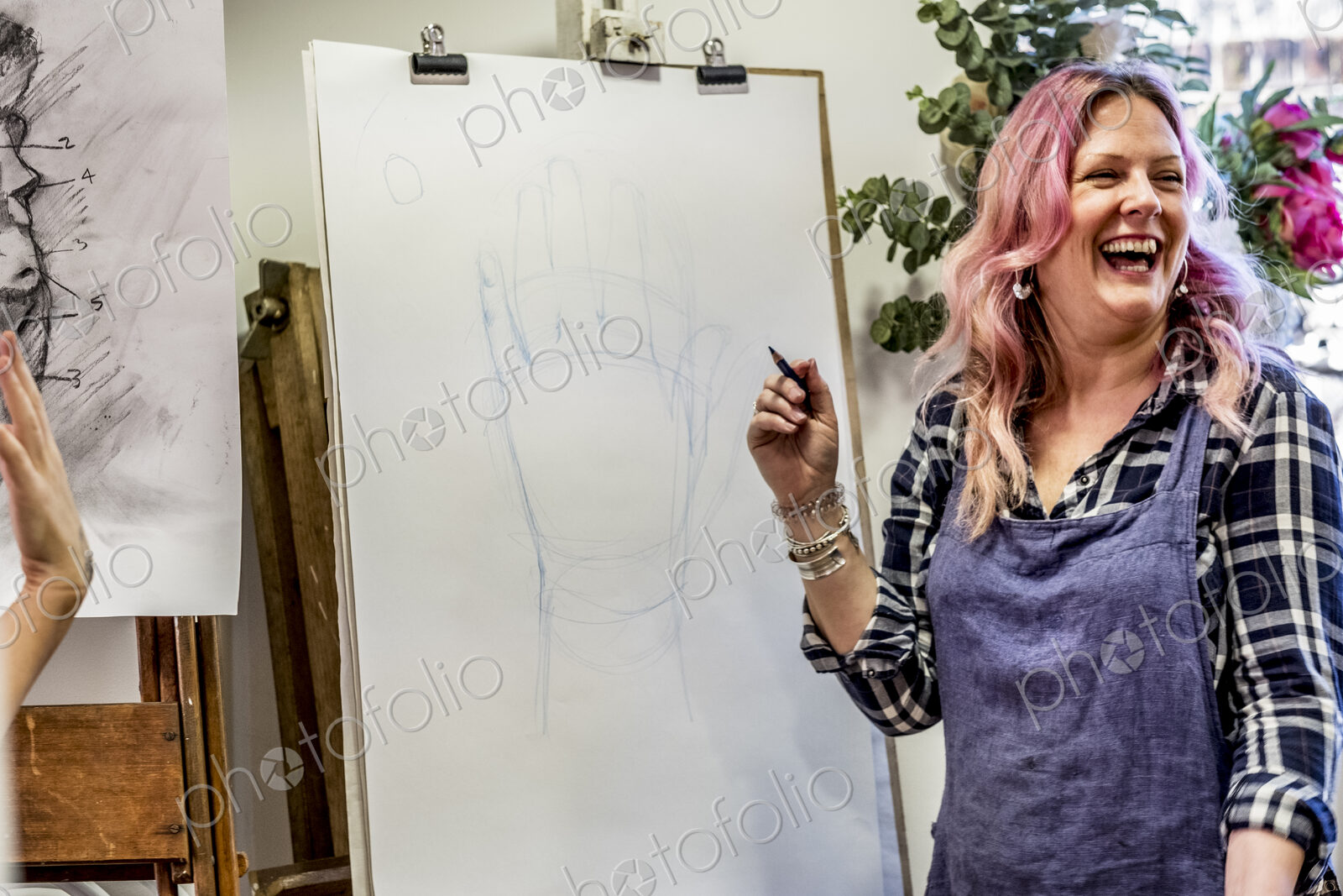 Laughing woman wearing apron standing at an easel, drawing of human hand.