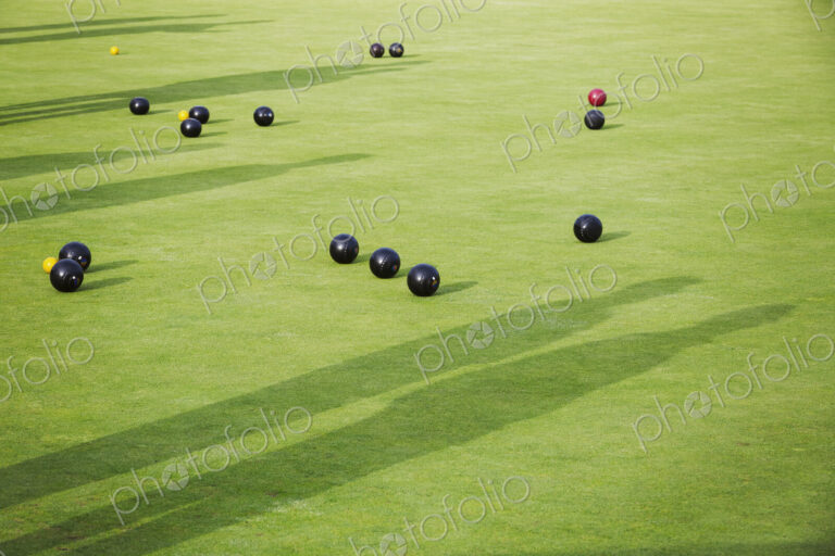 Lawn bowls balls scattered on the playing surface, two very close to the target jack…