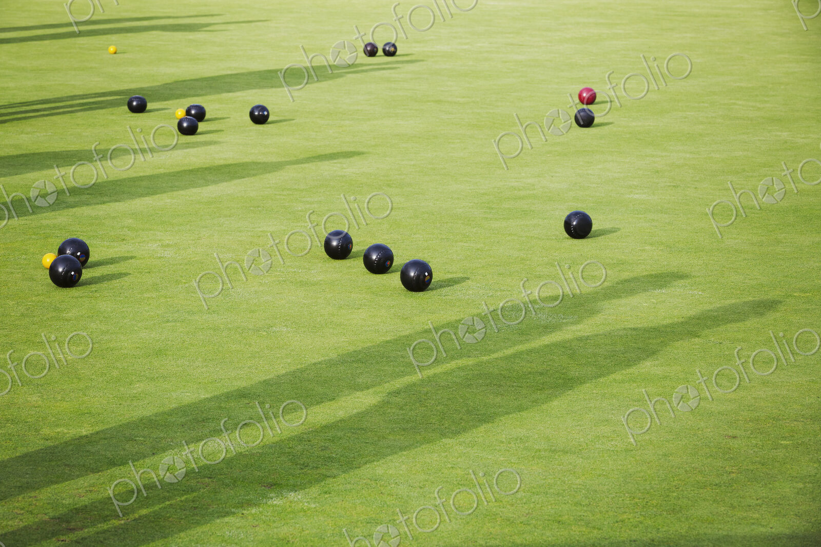 Lawn bowls balls scattered on the playing surface, two very close to the target jack…