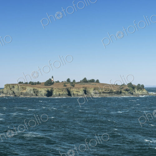 Lighthouse on an island in the sea off the Olympic Peninsula with Tatoosh mountains…