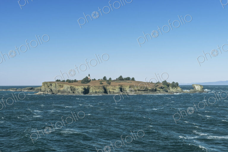 Lighthouse on an island in the sea off the Olympic Peninsula with Tatoosh mountains…