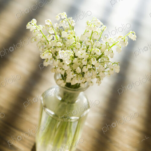 Lily of the valley flowers in glass vase on wooden table.