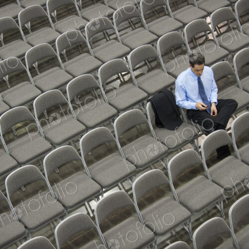 Lone businessman sitting alone in a room full of chairs, social distancing