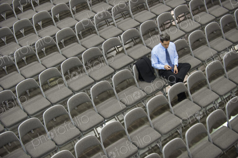 Lone businessman sitting alone in a room full of chairs, social distancing
