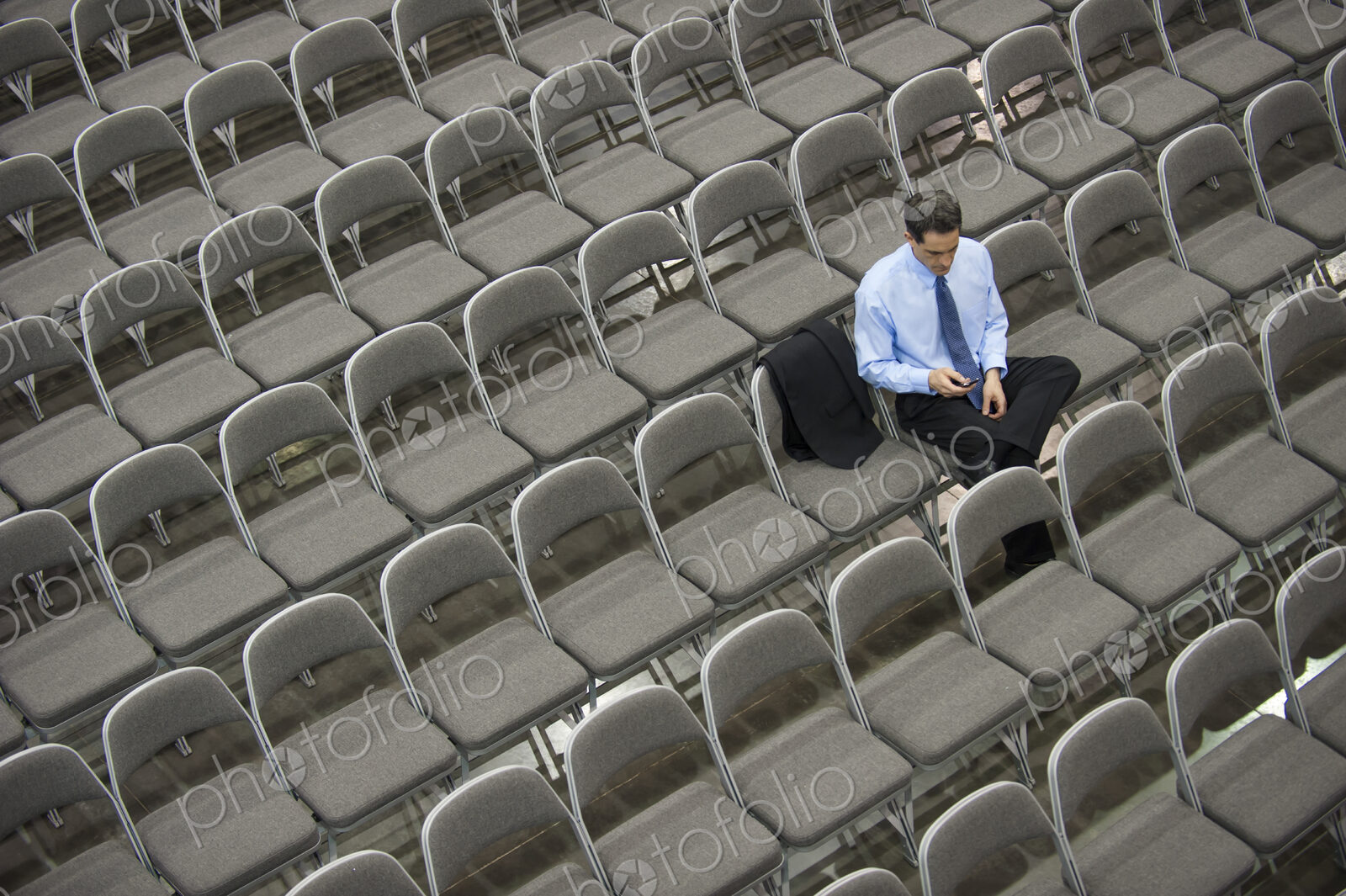 Lone businessman sitting alone in a room full of chairs, social distancing