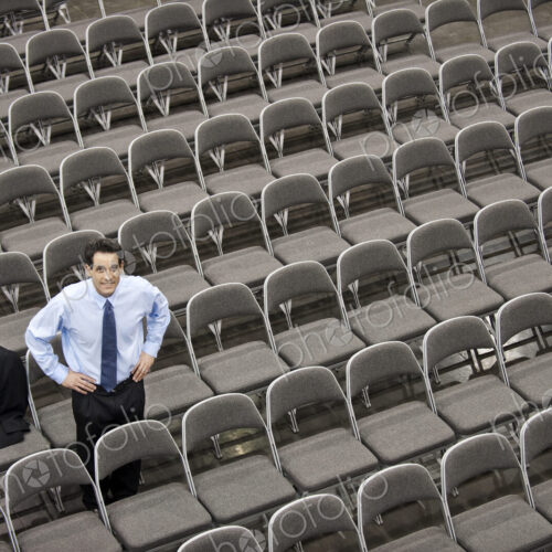 Lone businessman sitting alone in a room full of chairs, social distancing