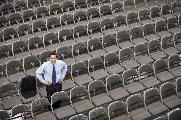 Lone businessman sitting alone in a room full of chairs, social distancing