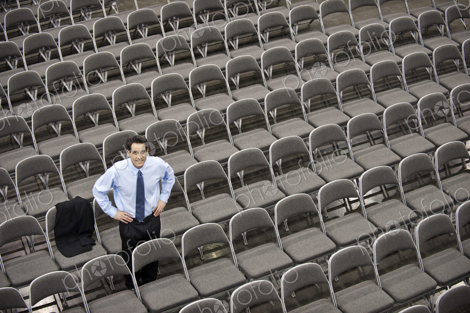 Lone businessman sitting alone in a room full of chairs, social distancing
