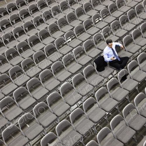 Lone businessman sitting alone in a room full of chairs, social distancing Lone businessman sitting alone in a room full of chairs, social distancing