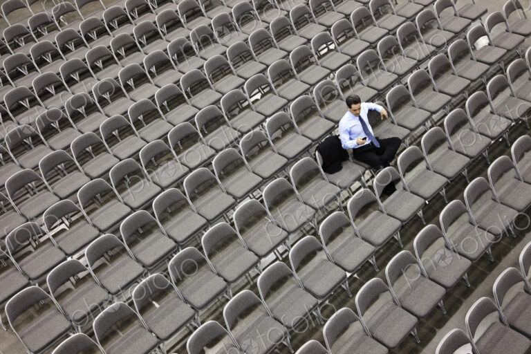 Lone businessman sitting alone in a room full of chairs, social distancing