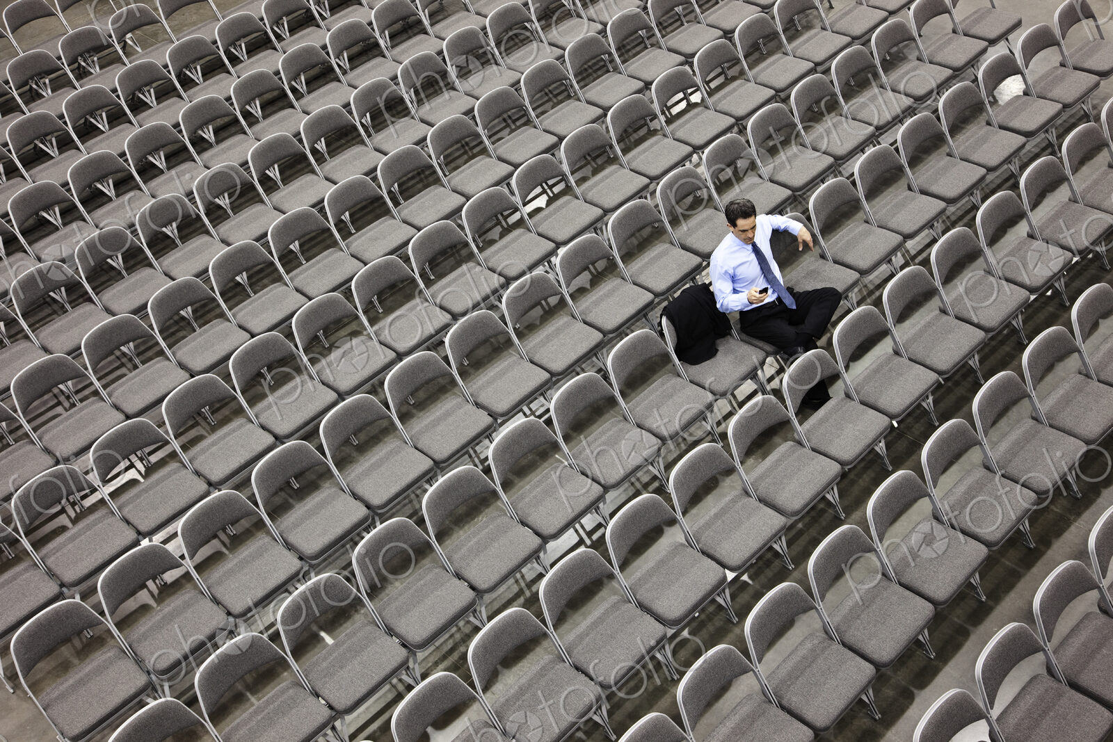 Lone businessman sitting alone in a room full of chairs, social distancing