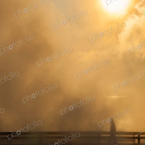 Lone figure walks along a steaming boardwalk at sunrise in Yellowstone's West Thumb… Lone figure walks along a steaming boardwalk at sunrise in Yellowstone's West Thumb…
