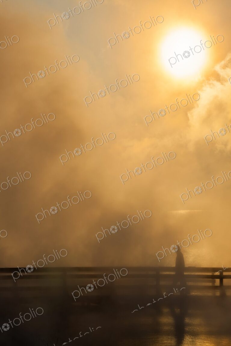 Lone figure walks along a steaming boardwalk at sunrise in Yellowstone's West Thumb…