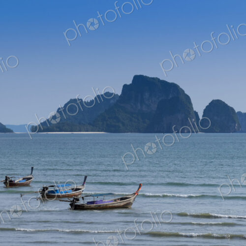 Long boats moored off the beach in Ao Nang with island beyond.