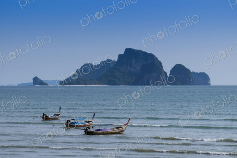 Long boats moored off the beach in Ao Nang with island beyond.