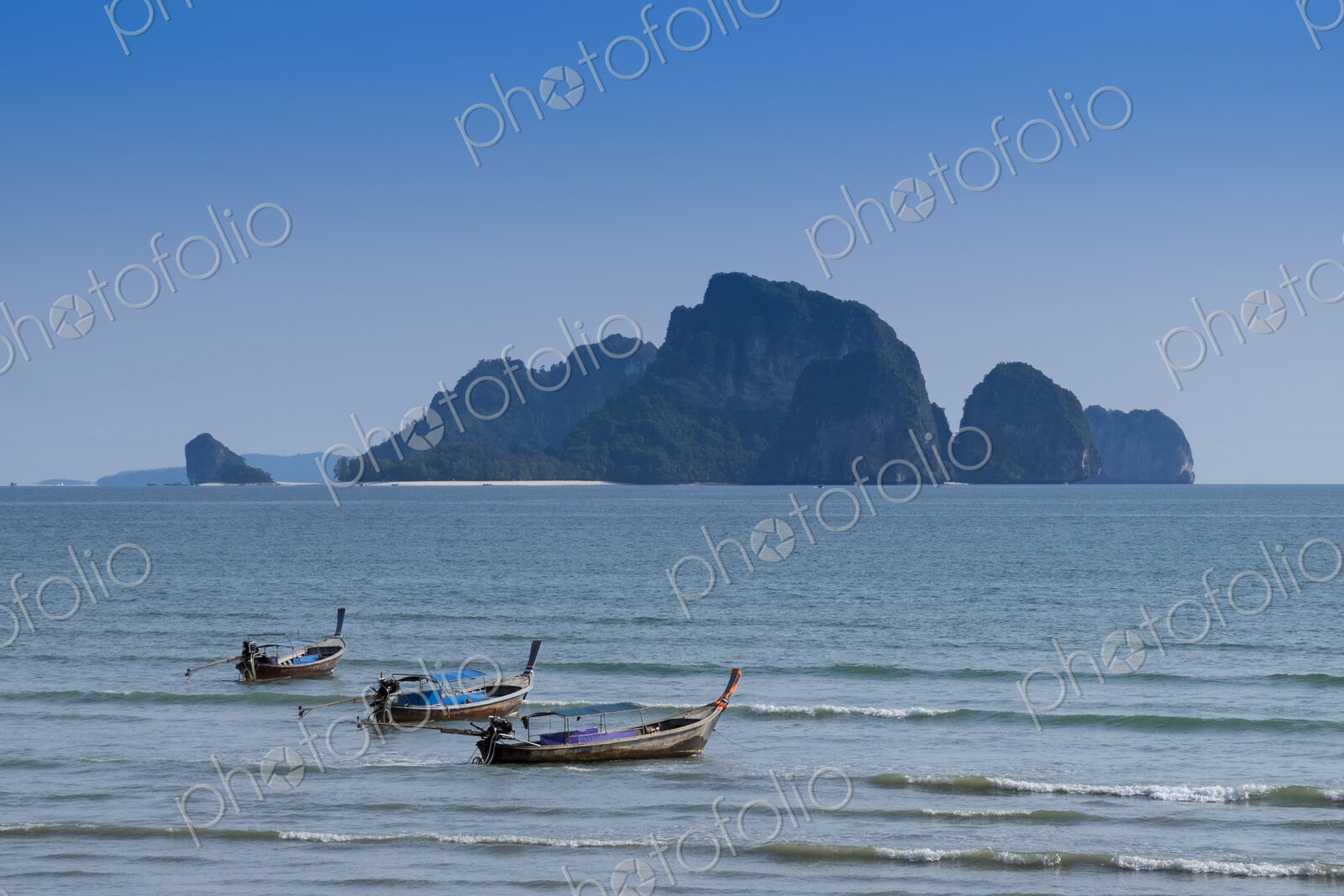 Long boats moored off the beach in Ao Nang with island beyond.