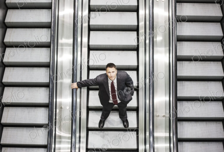 Looking down on a caucasian businessman looking up while riding an escalator in a…