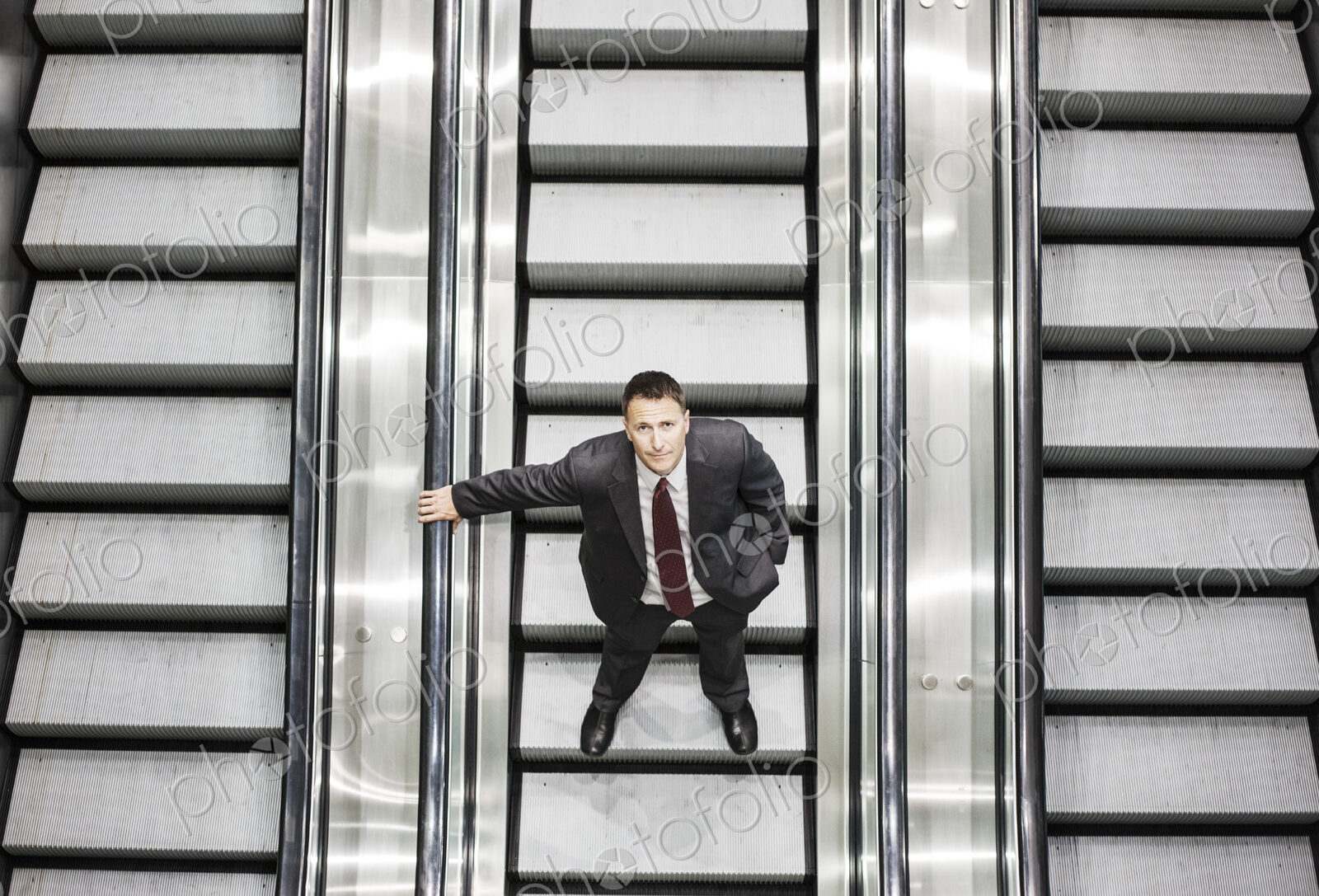 Looking down on a caucasian businessman looking up while riding an escalator in a…