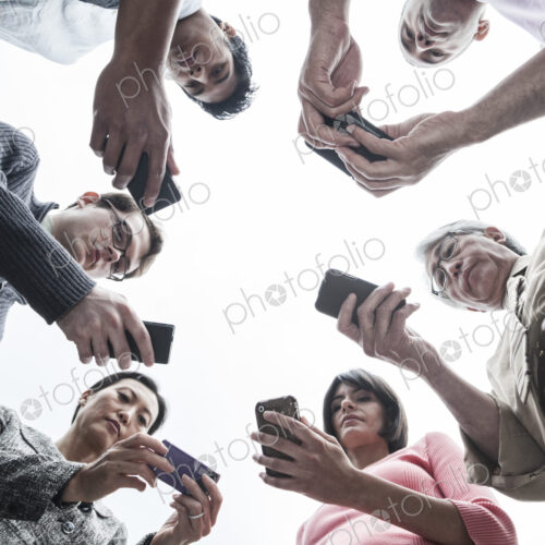 Looking up at a mixed race team of people looking at their cell phones. Looking up at a mixed race team of people looking at their cell phones.