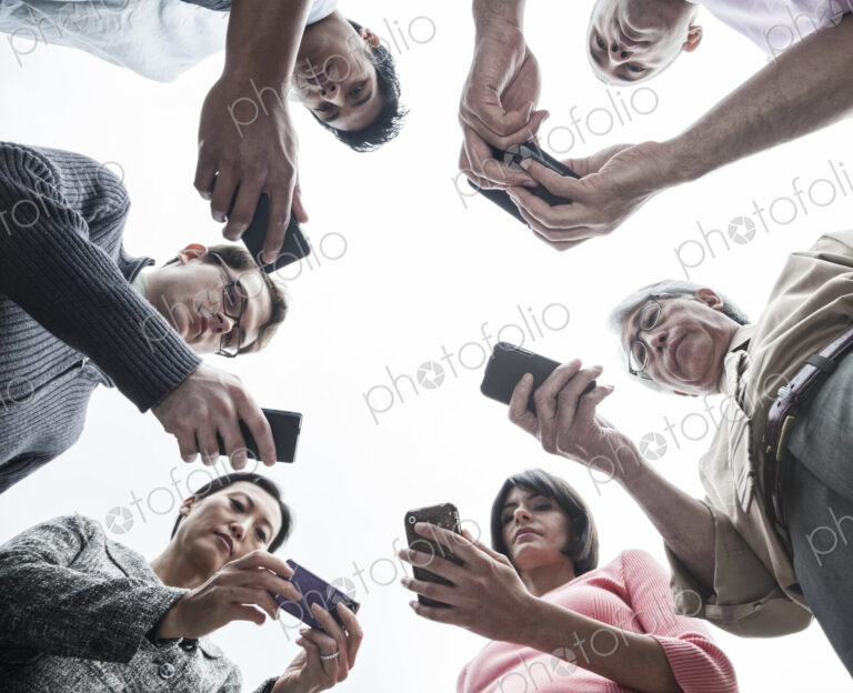 Looking up at a mixed race team of people looking at their cell phones.
