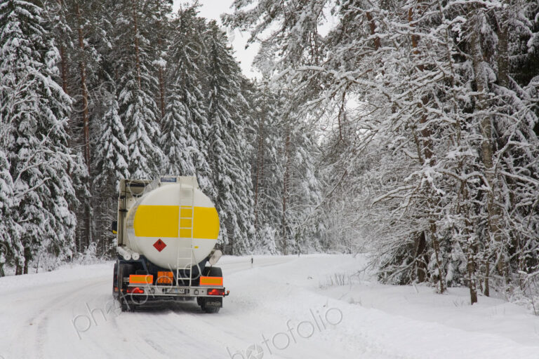 Lorry driving on snowy rural road through forest.