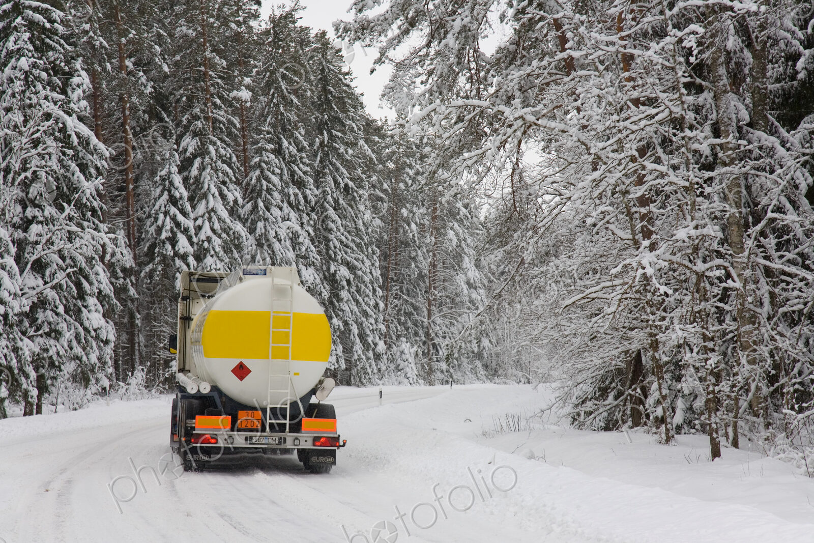 Lorry driving on snowy rural road through forest.