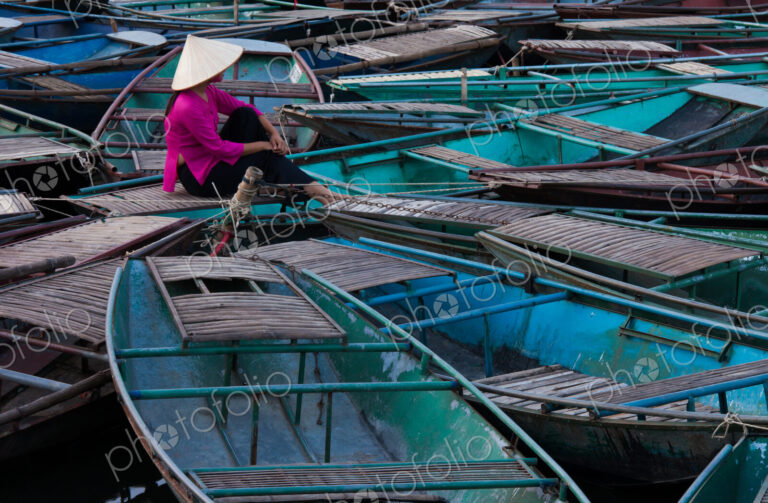 Lost in thought, a woman sits amidst a raft of boats. Ninh Binh, Vietnam