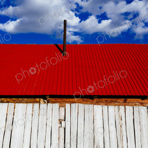 Low angle close up of white wooden building with bright red roof under a cloudy sky. Low angle close up of white wooden building with bright red roof under a cloudy sky.