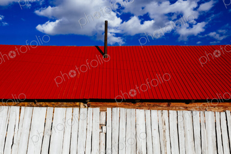 Low angle close up of white wooden building with bright red roof under a cloudy sky.