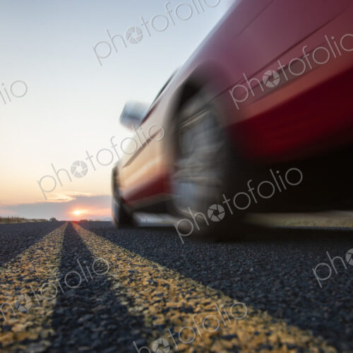Low angle view looking up at the side of a convertible sports car on the road at sunset.