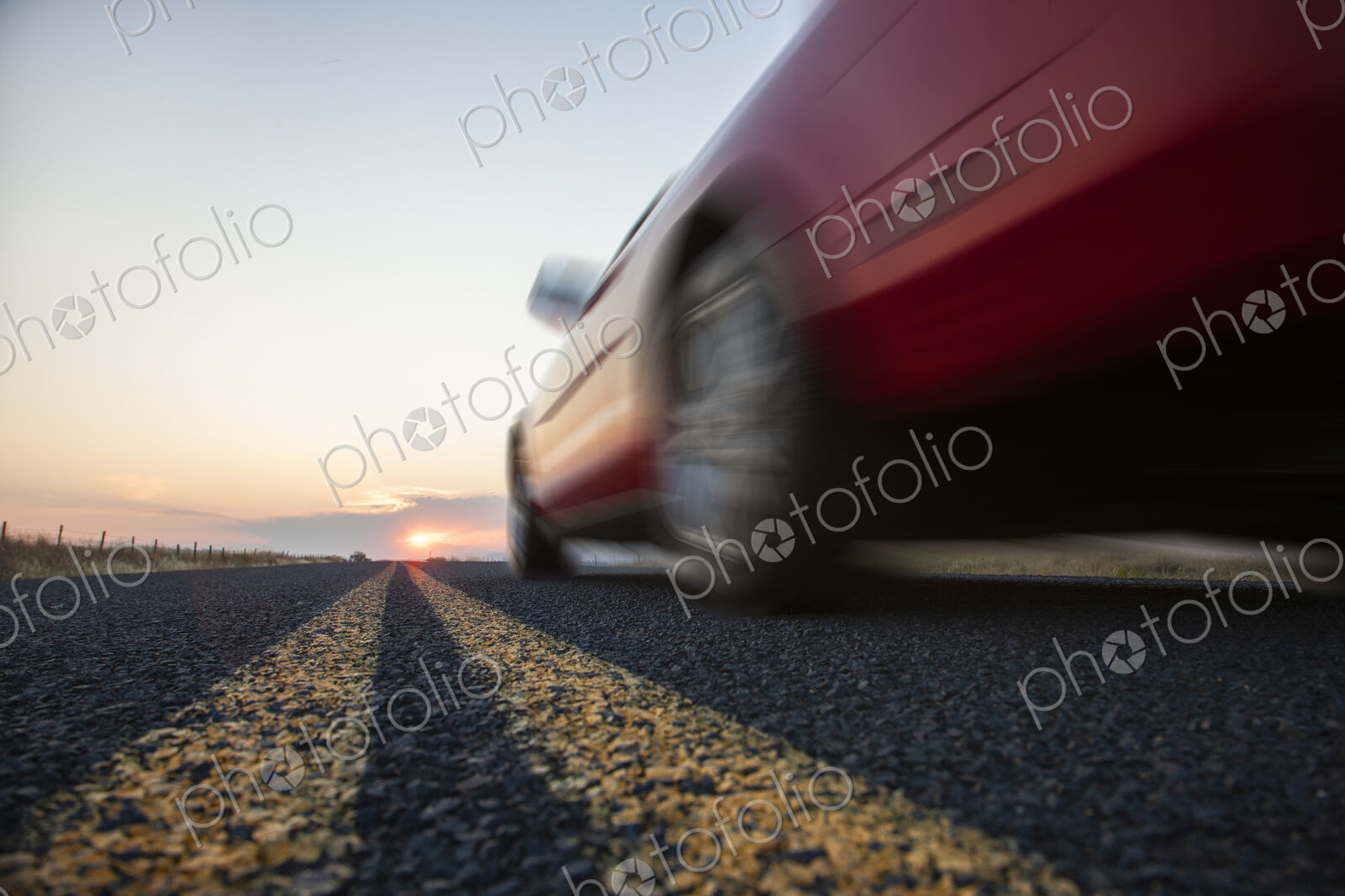 Low angle view looking up at the side of a convertible sports car on the road at sunset.