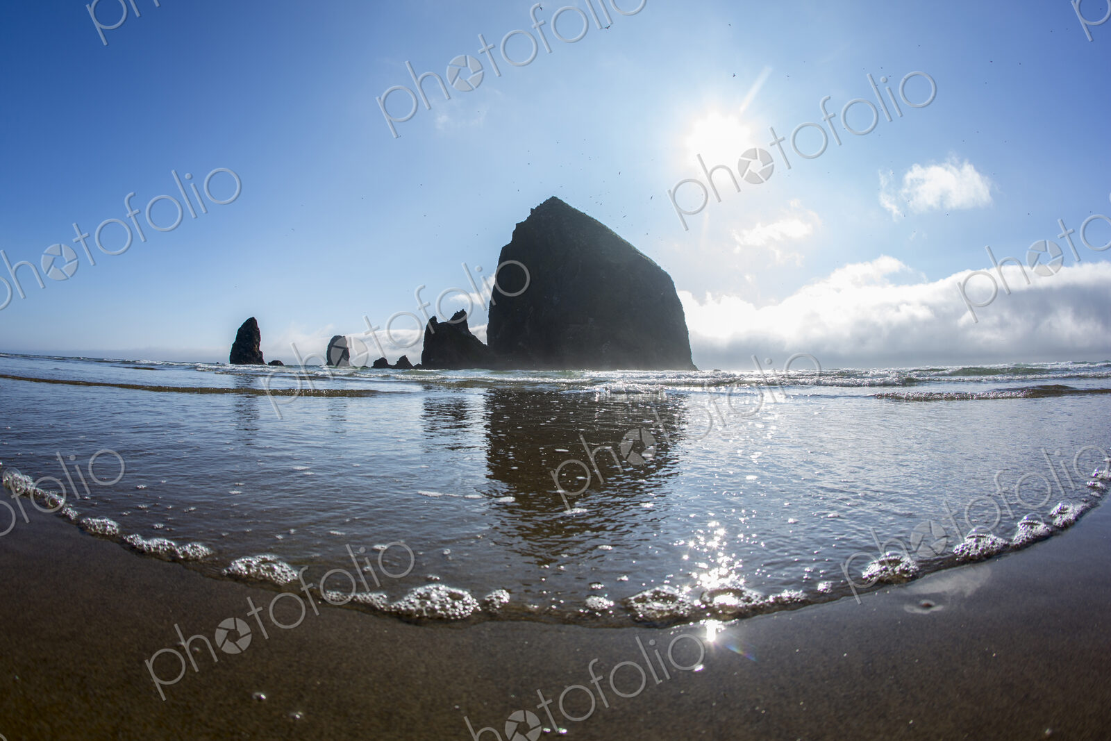 Low angle view of Haystack Rock reflecting in ocean waves, Cannon Beach, Oregon,…