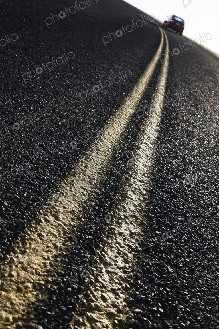 Low angle view of a double line on a highway and a car in the background.
